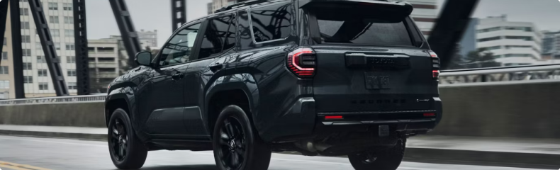 A dark gray Toyota 4Runner seen from behind crossing a city bridge