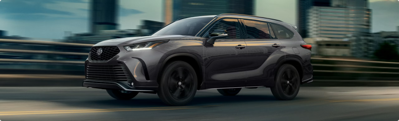 A dark gray Toyota Highlander driving through a city at dusk