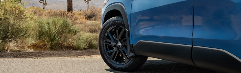 Close-up of the front wheel and black alloy rim of a blue Toyota Corolla Cross parked on a desert road