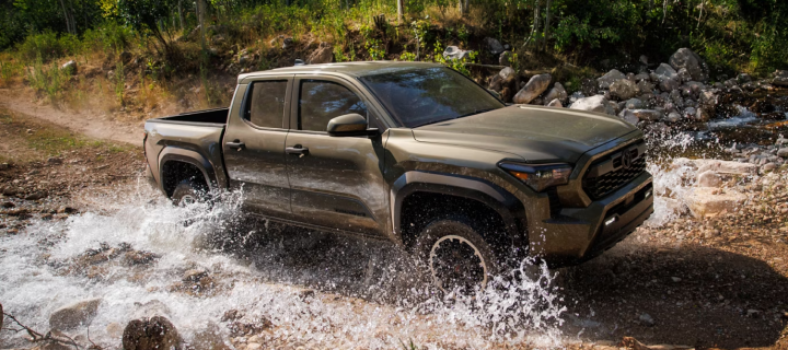 A green Toyota Tacoma splashing through a rocky creek crossing