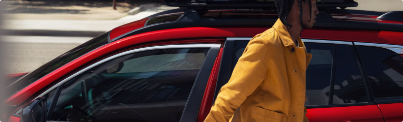 A man in a yellow jacket stepping out of a red Toyota with a roof cargo box