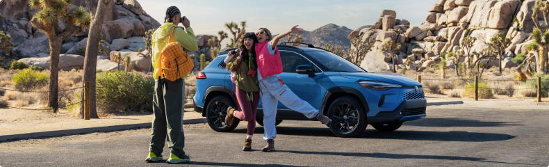 Three friends posing for photos beside a blue Toyota Corolla Cross Hybrid in a desert park