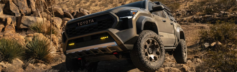 A tan Toyota Tacoma Trailhunter with amber fog lights climbing a rocky desert trail