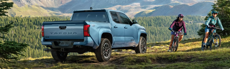 Two mountain bikers riding past a blue Toyota Tacoma parked on a grassy mountainside