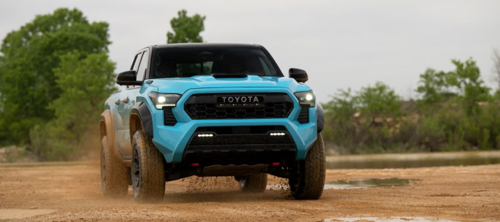 A light blue Toyota Tacoma TRD Pro driving head-on across a wet dirt trail