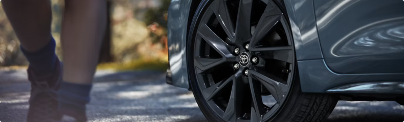 Close-up of a Toyota alloy wheel at the curb as a person walks past