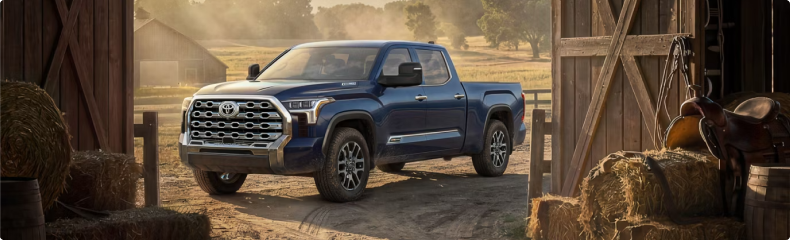 A blue Toyota Tundra parked in a barn doorway with hay bales and a saddle beside it