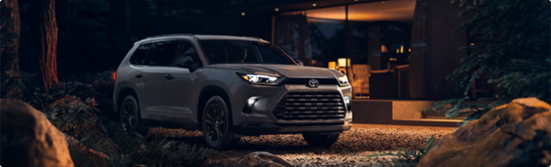 A silver Toyota Grand Highlander parked on a gravel drive outside a lit modern house at night