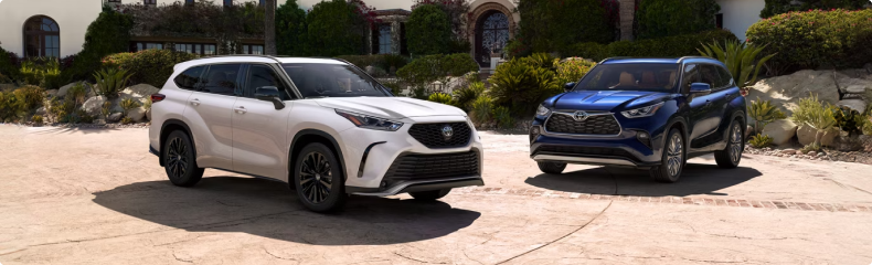 A white and a blue Toyota Highlander parked side by side on a landscaped driveway