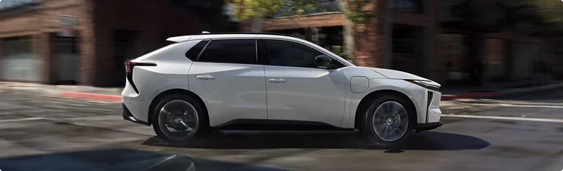 A white Toyota crossover in profile driving past brick storefronts