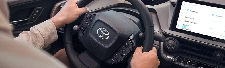 Close-up of hands on a Toyota steering wheel with the infotainment screen showing user profile settings