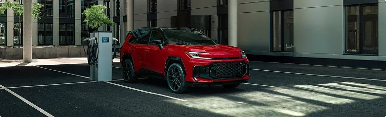 A red Toyota SUV parked beside a charging station outside a modern building