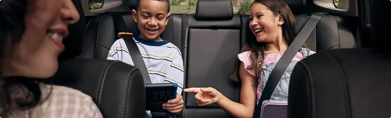 Two children laughing in the back seat of an SUV while an adult drives