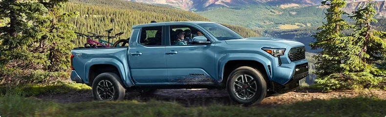 A blue Toyota Tacoma with bikes in the bed parked on a forest ridge above a mountain valley