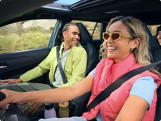 Two smiling friends riding in the front seats of a Toyota on a sunny day