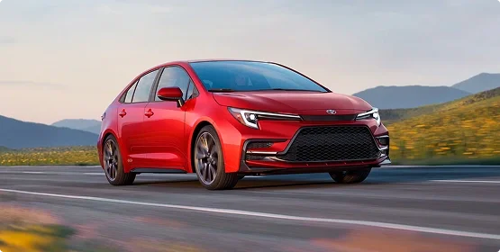 Red Toyota Corolla sedan driving on a highway past wildflower-covered hills