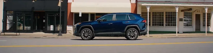 Dark blue Toyota RAV4 driving past storefronts on a small-town main street