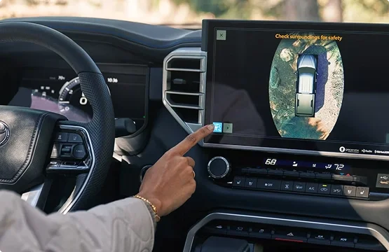 Driver tapping the camera view on the Toyota Tundra touchscreen showing an overhead view of the truck