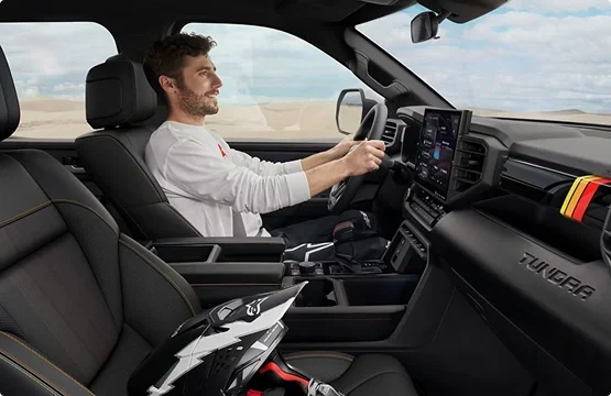 Smiling man driving a Toyota Tundra with a dirt bike helmet on the passenger seat