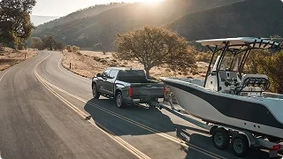 Gray Toyota pickup towing a center-console boat along a winding road at sunset