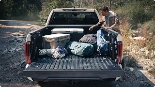 Man loading camping gear into the bed of a Toyota Tundra parked on a forest trail