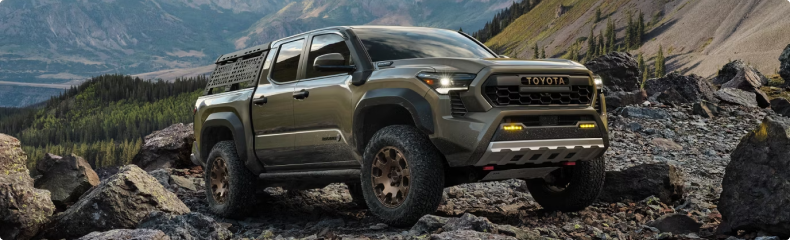 A green Toyota Tacoma Trailhunter with a bed rack parked on a rocky mountain trail