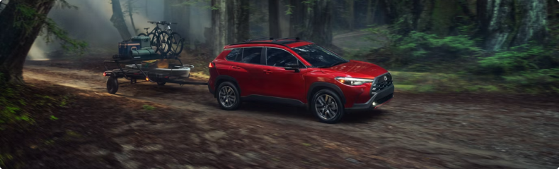 A red Toyota Corolla Cross towing a trailer loaded with bikes along a forest road