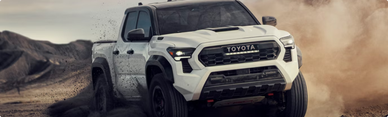 A white Toyota Tacoma TRD Pro kicking up dust on a desert trail