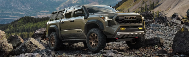 A green Toyota Tacoma Trailhunter with a bed rack parked on a rocky mountain trail