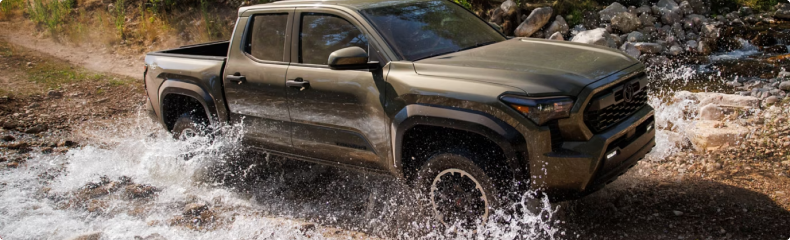 A green Toyota Tacoma splashing through a rocky creek crossing