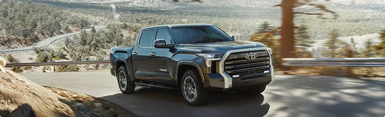 A dark gray Toyota Tundra on a winding mountain road lined with snow-dusted pines