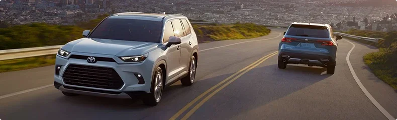 Two light blue Toyota SUVs on a curving highway above a city at dusk