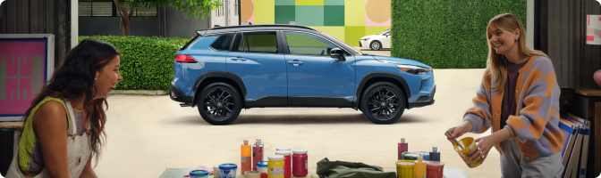 Blue 2026 Toyota Corolla Cross Hybrid parked behind two people at an outdoor craft table