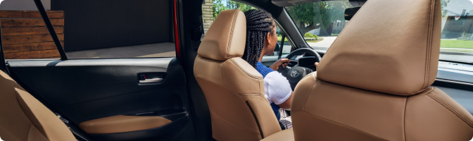 Driver seated behind the wheel of a 2026 Toyota Corolla Cross, seen past the tan front seats