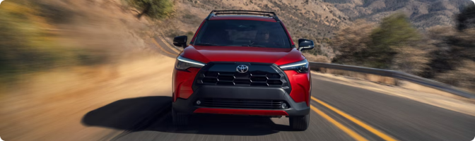Red 2026 Toyota Corolla Cross driving toward the camera on a winding mountain road