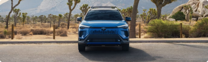 Blue 2026 Toyota Corolla Cross Hybrid, front view, parked on a desert road lined with Joshua trees