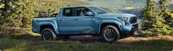 Blue 2026 Toyota Tacoma Double Cab parked on a forested hillside with mountain bikes in the bed