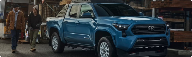 Blue 2026 Toyota Tacoma Double Cab parked outside a lumber yard as shoppers walk past