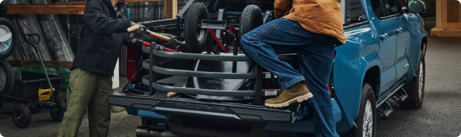 Two people loading gear into the bed of a blue 2026 Toyota Tacoma with the tailgate down