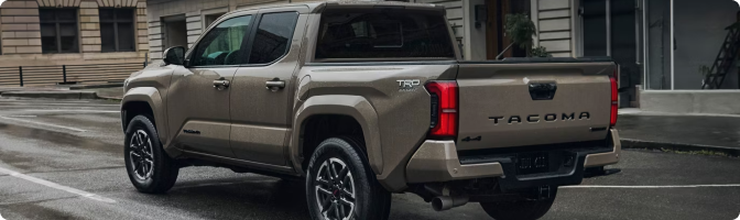 Rear view of a tan 2026 Toyota Tacoma Double Cab on a wet city street