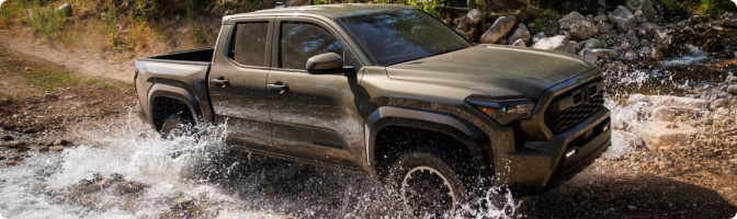 Green 2026 Toyota Tacoma splashing through a shallow creek crossing